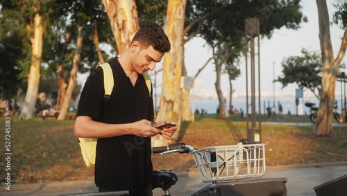 Mixed race young man takes bike bicycle in sharing parking lot, phone application for rent bike.