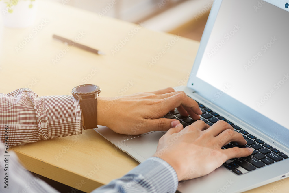 Fototapeta premium Asian businessman working on his laptop computer with blank copy space screen he typing on keyboard at home office desk. The man play social media on computer table