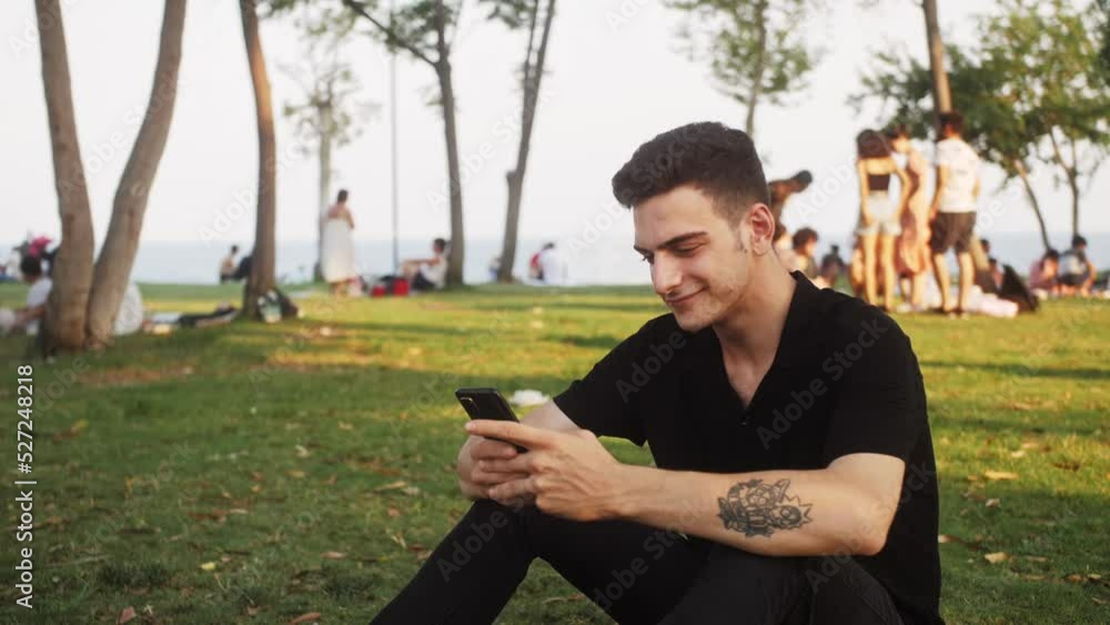 Student Palestinian descent sitting on the grass at the university campus. Mixed race guy uses smartphone at the urban park. Student Palestinian descent sitting on the grass at the university campus. Mixed race guy uses smartphone at the urban park.