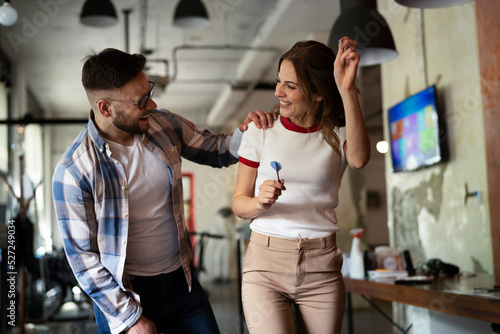 Young colleagues taking break after work. Happy young businessman and businesswoman playing darts in the office