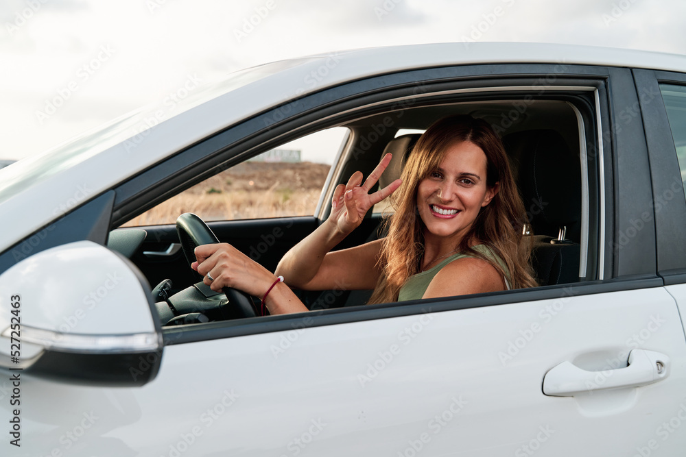 Young woman waving through the window while driving her car