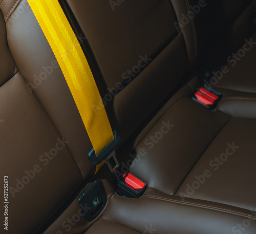 Automobile leather seat of a modern luxury car with a yellow safety belt. Yellow seat belt in a sports car close-up, blurry background. Brown leather car seat. Fasten your seat belts.