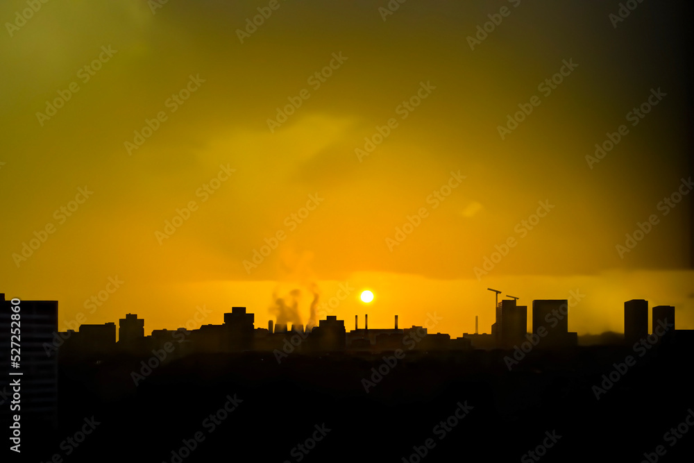 Golden sunset in the big city. Silhouettes of houses, industrial facilities - cooling towers, pipes, crane, houses and buildings of different heights. Beautiful sky, evening cityscape. Wallpaper