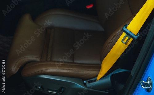 Automobile leather seat of a modern luxury car with a yellow safety belt. Yellow seat belt in a sports car close-up, blurry background. Brown leather car seat. Fasten your seat belts.