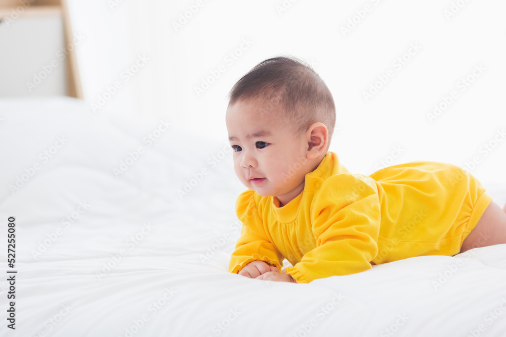 Portrait of beautiful young Asian newborn little baby prone on the bed at home, Happy baby smile wears a yellow shirt relaxing in the room, Family morning at home Portrait of beautiful young Asian newborn little baby prone on the bed at home, Happy baby smile wears a yellow shirt relaxing in the room, Family morning at home