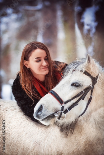A girl in a winter forest. A girl and a pony. A girl in red and a white pony.