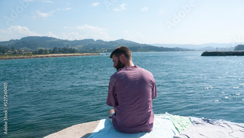 Hombre barbudo blanco sentado en dique de un lago photo