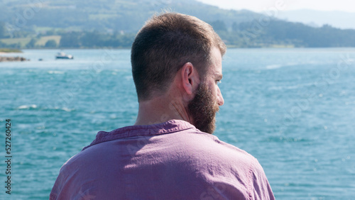 Hombre barbudo blanco sentado en dique de un lago