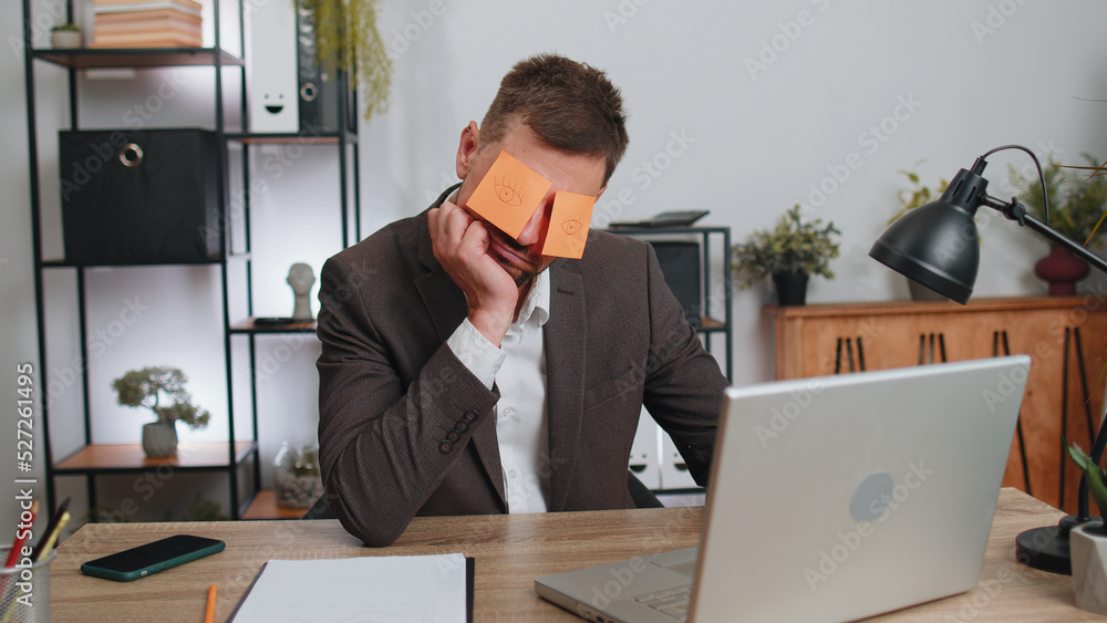 Inefficient tired businessman in suit working sleeping on laptop computer with eyes stickers on face at office workplace desk. Funny lazy manager freelancer man. Business people. Cheating to sleep Inefficient tired businessman in suit working sleeping on laptop computer with eyes stickers on face at office workplace desk. Funny lazy manager freelancer man. Business people. Cheating to sleep