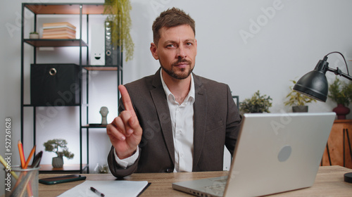 Photos Businessman in suit working on laptop computer shakes finger and saying no, be careful, scolding and giving advice to avoid danger mistake, disapproval sign at office