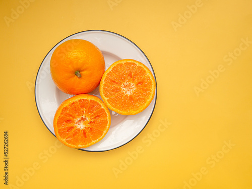 Top view of fresh oranges on a white plate over a yellow background