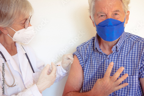 Doctor giving injection to senior caucasian man, old retired receiving booster of covid 19 vaccine, people wearing mask