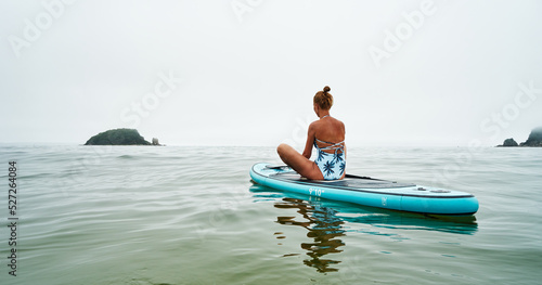 A girl in a swimsuit on a SUP board performs yoga exercises in the calm waves of the morning sea. Spiritual healing.