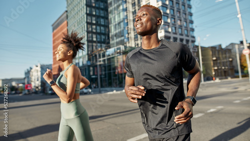 Smiling black sports couple running on city street