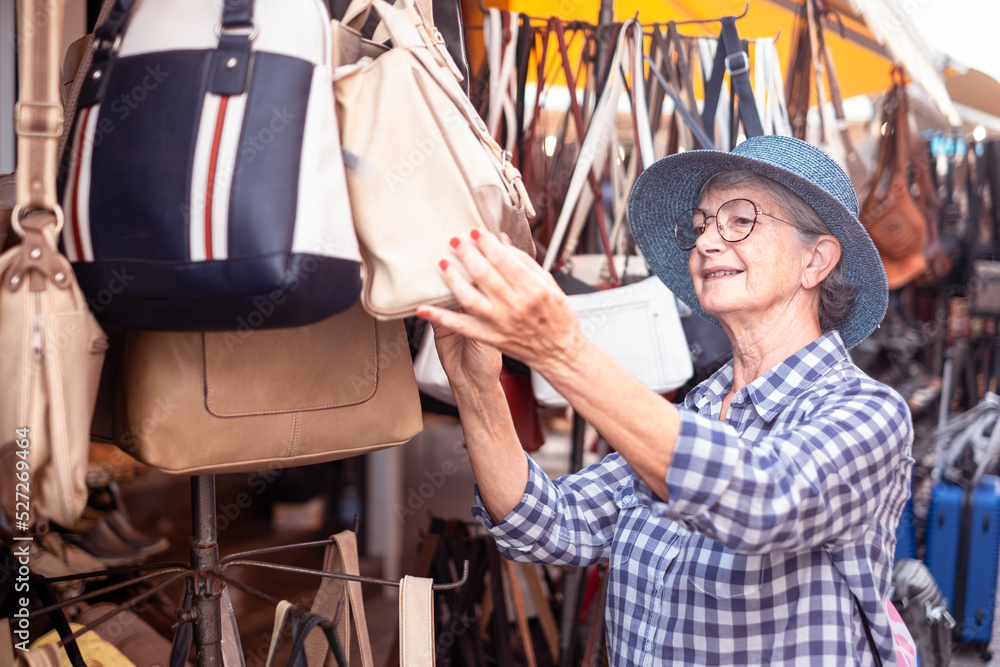 Fototapeta premium Smiling senior woman in blue hat choosing a bag in a store
