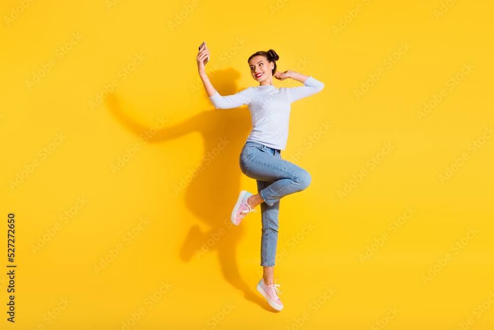 Full length photo of sweet cute girl dressed white shirt recording video jumping high isolated yellow color background