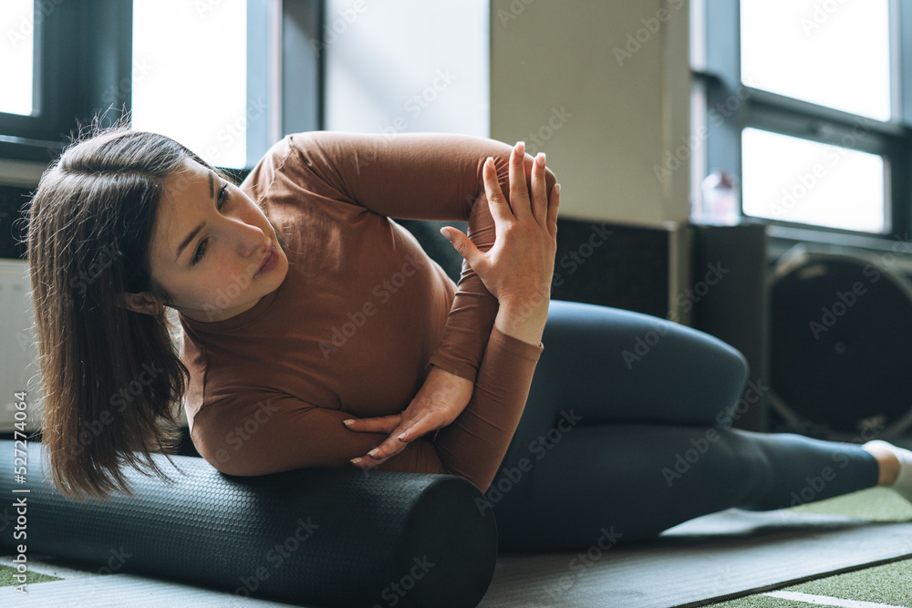 Young brunette woman doing stretching pilates on massage roll in fitness club gym Young brunette woman doing stretching pilates on massage roll in fitness club gym