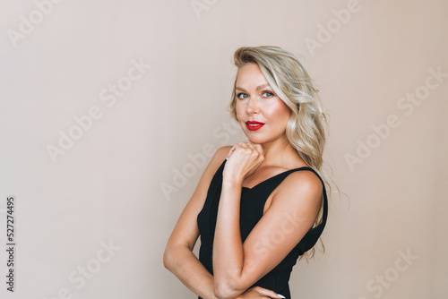 Portrait of gorgeous beautiful blonde young woman with bright makeup in evening dress on beige background