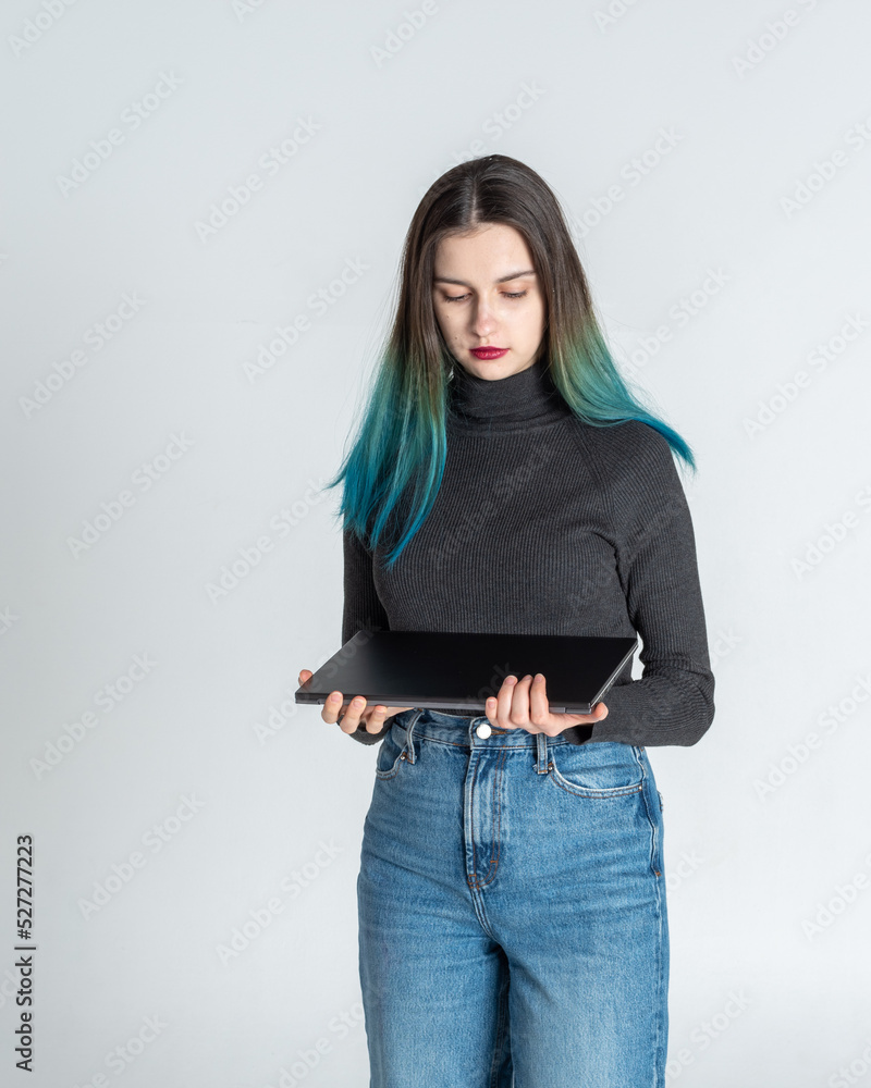 A thoughtful serious young woman with blue hair is a university college student holding a laptop isolated against a gray studio background. Happy Asian girl with laptop thinking A thoughtful serious young woman with blue hair is a university college student holding a laptop isolated against a gray studio background. Happy Asian girl with laptop thinking
