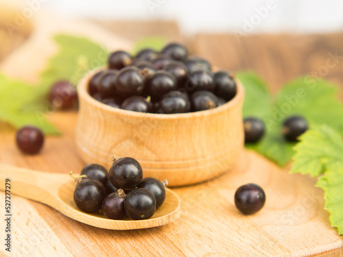 Fresh blackcurrant berries in a bowl on a wooden table near green leaves. Juicy natural currant fruits. Black currant