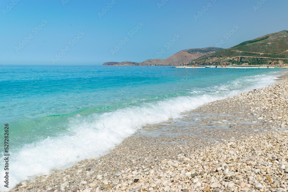 Pebble long Borsh beach with clear blue water. Cloudless sky. Albania. Ionian Sea. Pebble long Borsh beach with clear blue water. Cloudless sky. Albania. Ionian Sea.