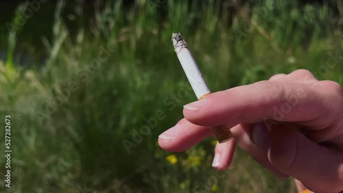 Man is holding white cigarette in his hand in forest. Harmful habit for health and pollution of the environment.