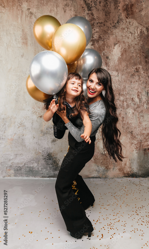 Charming mom and little daughter in the same outfit pose together after a birthday party. Portrait of a charming girl hugging her daughter. balloons