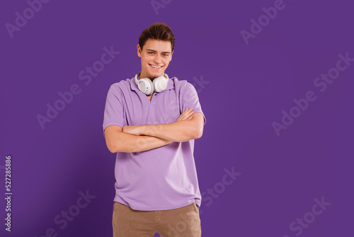 Happy smiling handsome young man with headphones enjoying cool music, posing isolated on violet studio background. Copy space. © neonshot