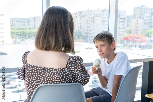 A cute happy little schoolboy boy is talking to his mother sitting at a table in a cafe against window. Mom talks to her son about school. The babysitter talks confidentially with the teenager. photo