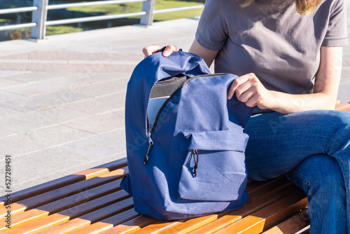Women's hands zip up an orange school backpack with school supplies, books, an office, a laptop, on a park bench. The concept of Back to School.