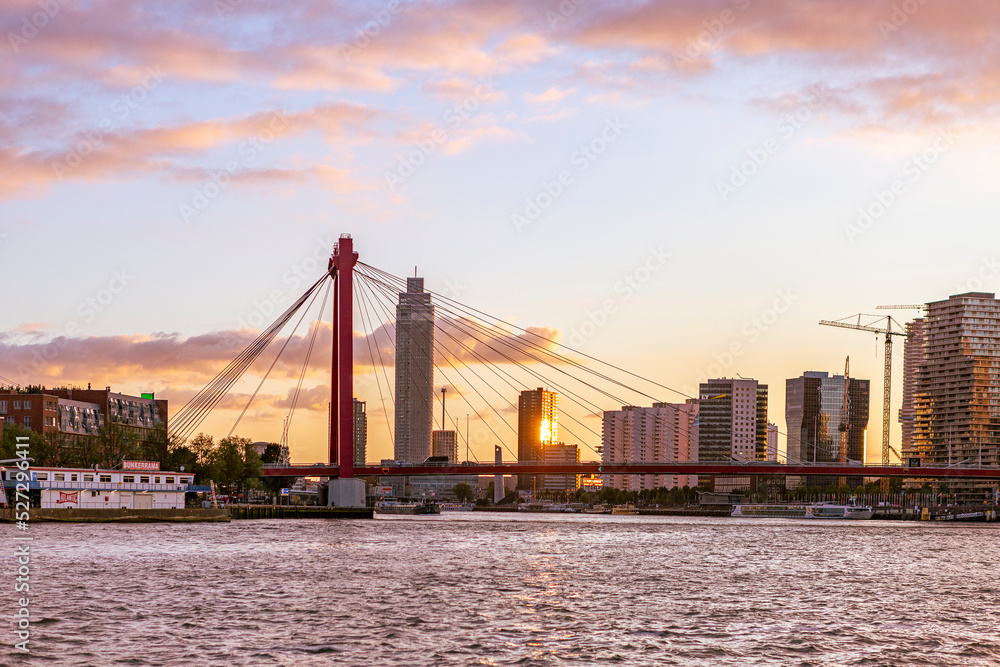 Bright sunset skyline of orange cable bridge and the Erasmus bridge and Euromast in the background with dramatic clouds
