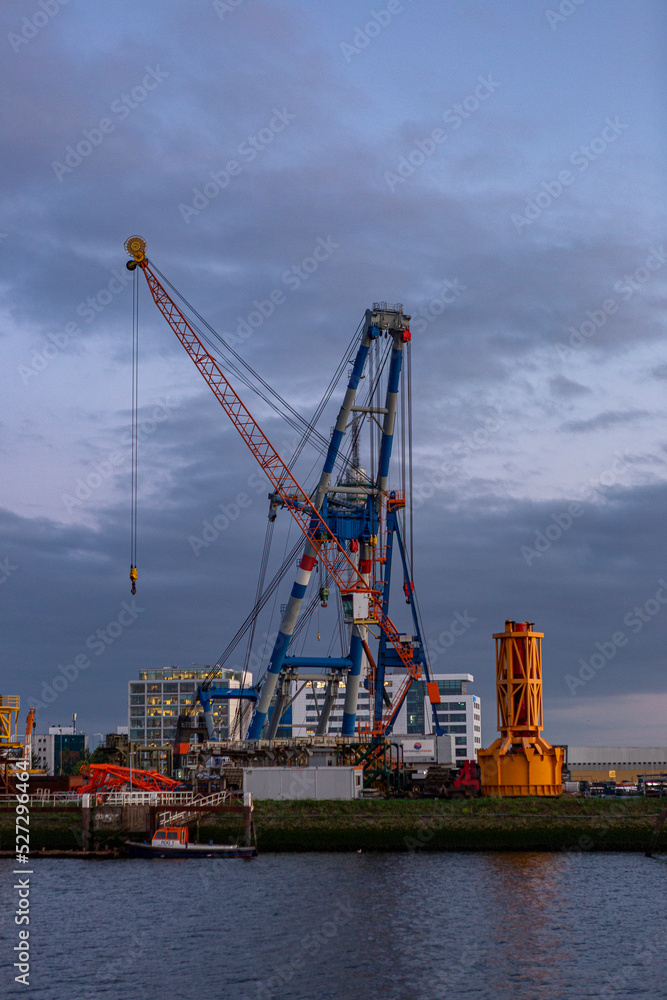 Vertical frame of industrial inland shipping colourful cranes in port at sunset blue hour. Engineering heavy machinery architecture and logistics concept