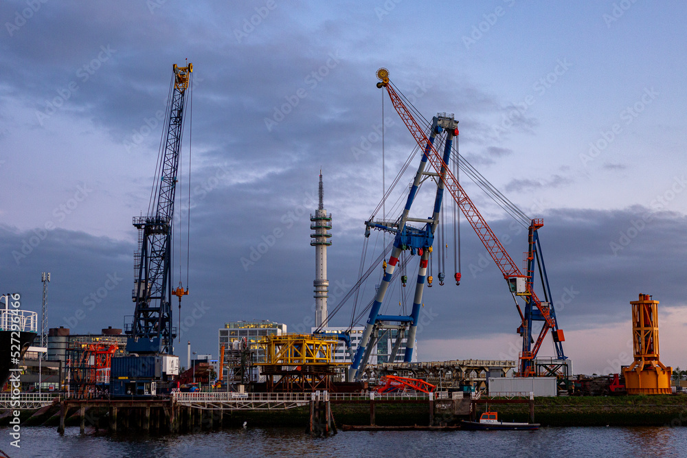Large industrial inland shipping vessel boat in port at anchor with cranes and lights in the evening at sunset blue hour