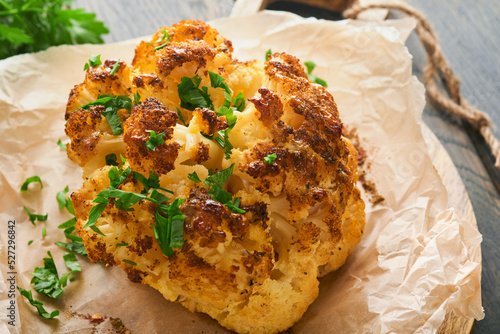 Baked cauliflower. Oven or whole baked cauliflower spices and herbs server on wooden rustic board on old wooden vintage table background. Delicious cauliflower. Eyal Shani dish. Perfect tasty snack. photo