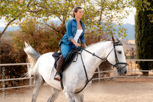 side view of a girl riding white horse in stable in summer photo