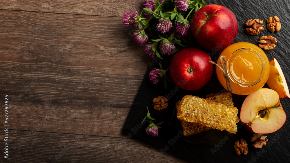 Mason jar with honey, honeycomb, red apples and walnuts on kitchen table