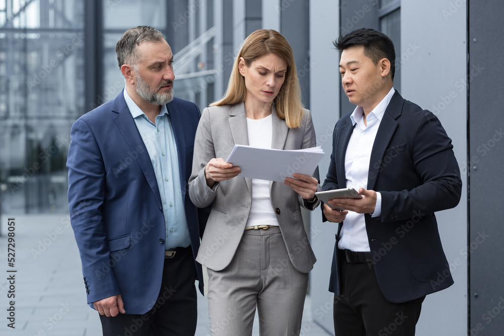 Diverse business team three colleagues employees discuss documents contract outside office building businessman and businesswoman holding bills and financial reports talking Diverse business team three colleagues employees discuss documents contract outside office building businessman and businesswoman holding bills and financial reports talking