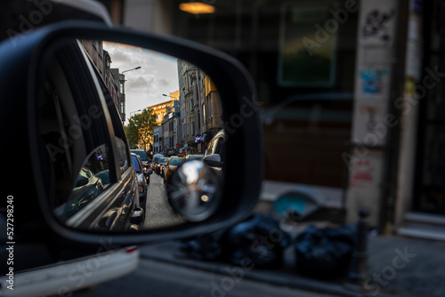 reflection of huge traffic in the right car mirror in the evening at sunset in a city of a million people with garbage on the sidewalk. Traffic.