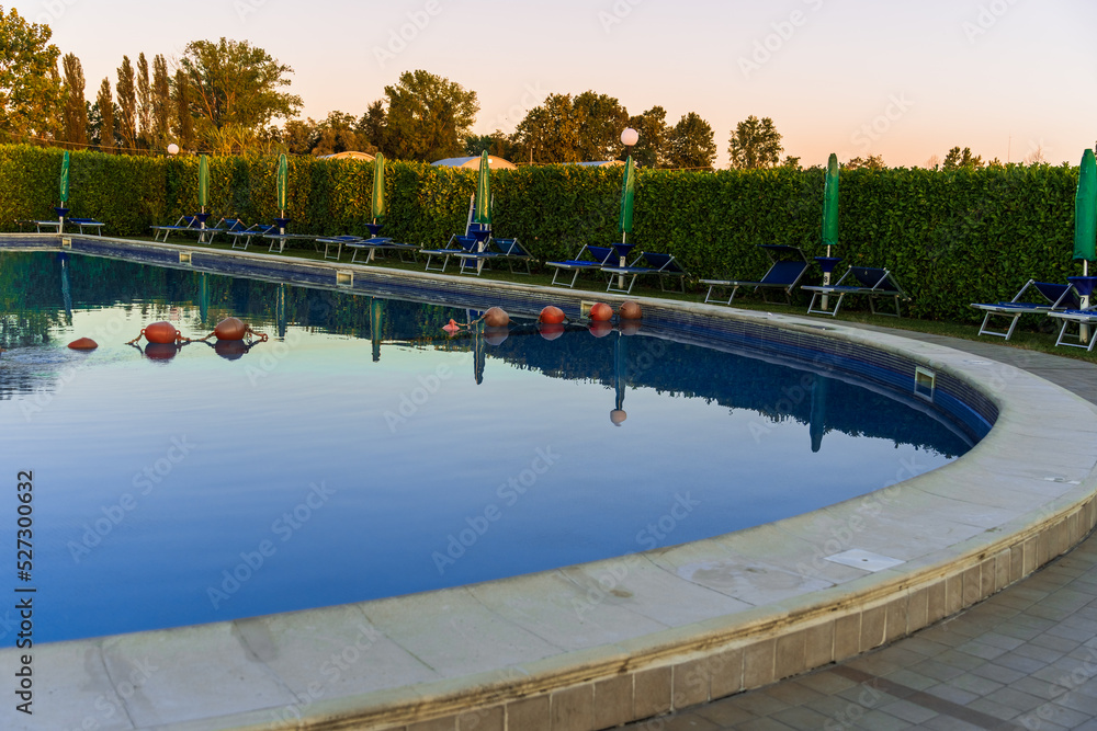 Fototapeta premium The blue sky is reflected on the surface of the outdoor pool, the summer beautiful pool in the hotel, comfortable summer vacation in Italy, the play of reflections on the surface of the water