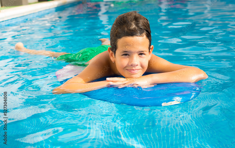 Cute smiling boy paddling on the surf board in pool