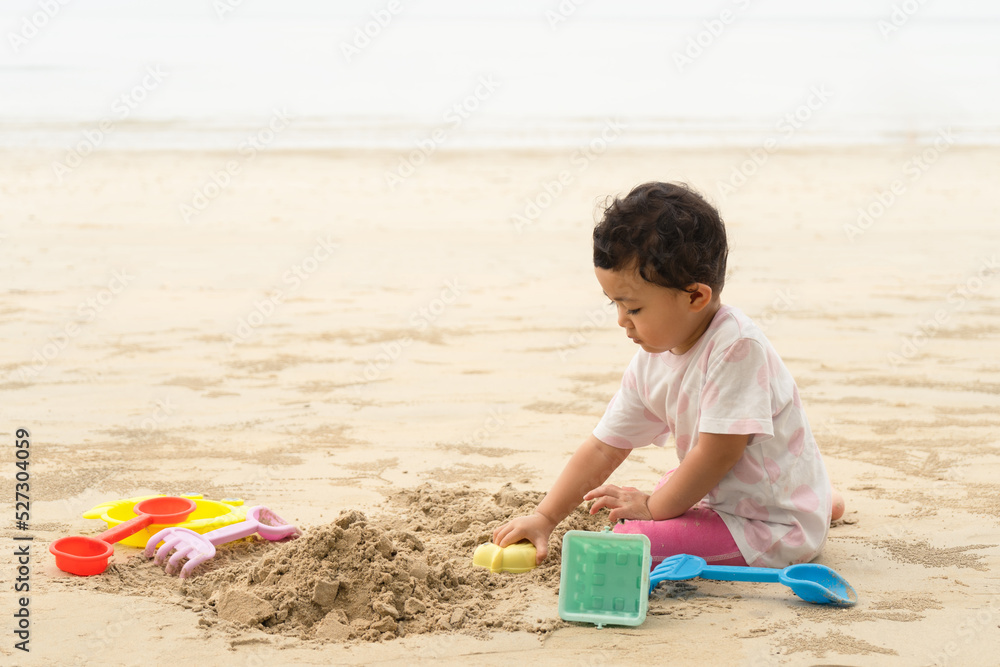 Cute asian baby girl playing with beach toys and sand on tropical beach. Summer time and girl on beach. Cute asian baby girl playing with beach toys and sand on tropical beach. Summer time and girl on beach.