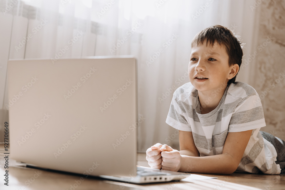 Teenager boy in lying on floor with laptop, having video call and online lesson at home. Schoolboy studying homework. Distance education, remote training concept. Teenager boy in lying on floor with laptop, having video call and online lesson at home. Schoolboy studying homework. Distance education, remote training concept.