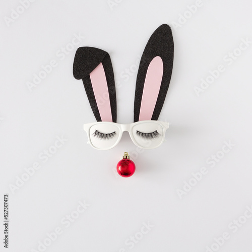 Christmas Bunny face made of black fabric ears with sunglasses and red christmas ball on white background. Happy New Year minimal concept.
