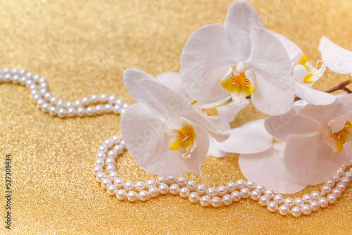 white Orchid and pearl necklace on a shiny gold background 