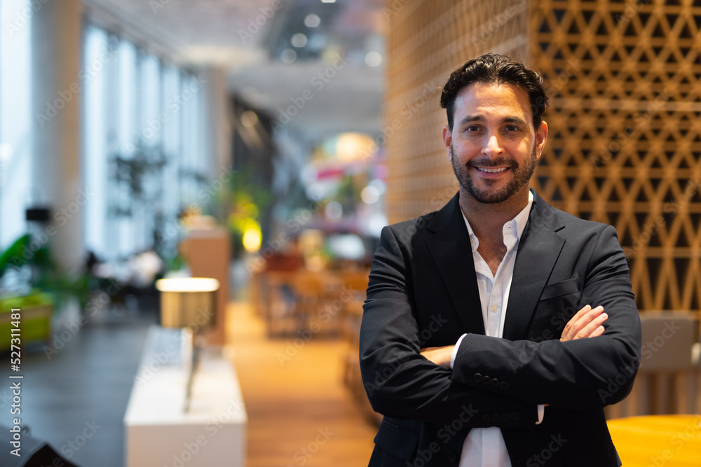 Fototapeta premium Portrait of happy handsome Hispanic businessman at coffee shop with arms crossed