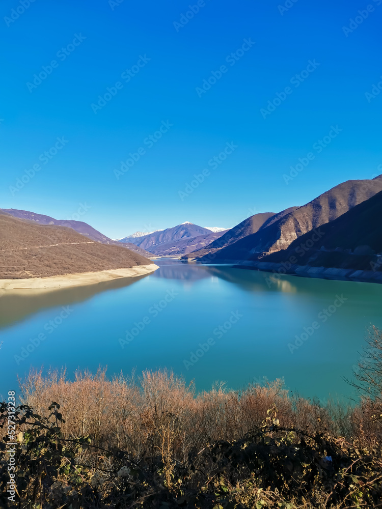 The Ananuri River is country of Georgia surrounded by mountains. Amazing view mountain lake on sunny winter day. Snowy peaks of mountains against the background of water. Gorgeous nature landscape