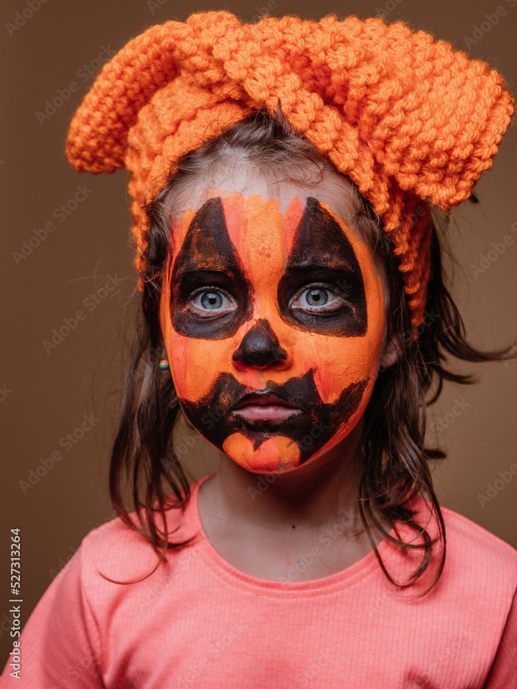 Elementary child with an orange bow on his head dressed as a pumpkin with big wide blue eyes stares Elementary child with an orange bow on his head dressed as a pumpkin with big wide blue eyes stares