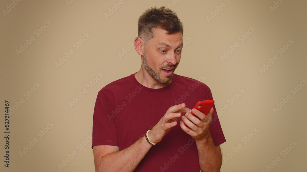 Happy excited joyful young man use smartphone typing browsing say wow yes, found out great big win news doing winner gesture. Adult stylish male guy isolated on beige studio wall background indoors Happy excited joyful young man use smartphone typing browsing say wow yes, found out great big win news doing winner gesture. Adult stylish male guy isolated on beige studio wall background indoors
