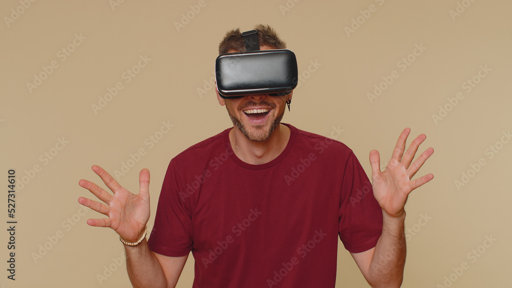 Bearded handsome young man using headset helmet app to play simulation drawing game. Watching virtual reality 3D 360 video. Adult male guy in VR goggles isolated on beige studio background indoors Bearded handsome young man using headset helmet app to play simulation drawing game. Watching virtual reality 3D 360 video. Adult male guy in VR goggles isolated on beige studio background indoors