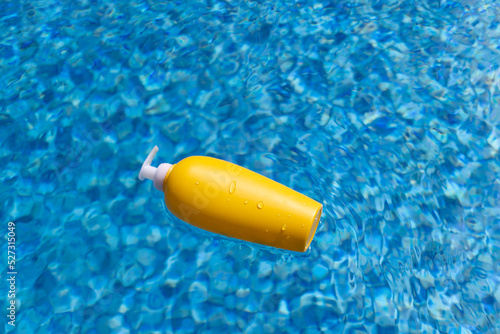 Sunscreen bottle floating in blue water of swimming pool.